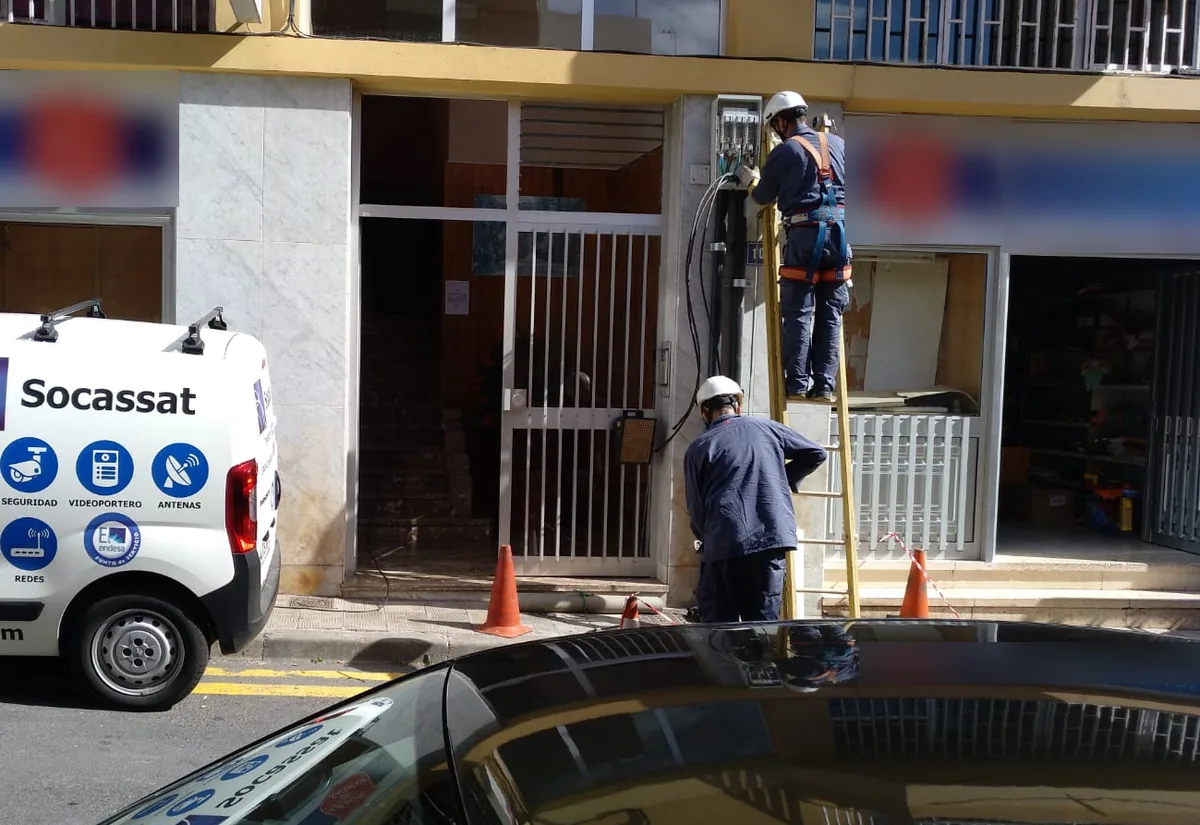 Técnicos de Socassat trabajando en la caja de una acometida eléctrica en la fachada de un edificio, con la furgoneta de la empresa