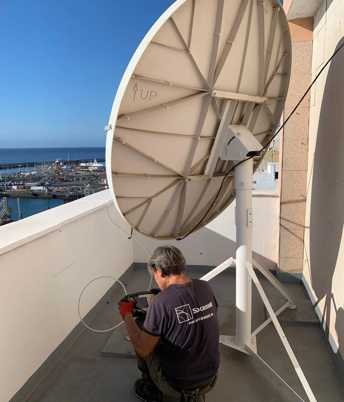 Antenista de Socassat ajustando una parabólica de gran diámetro sobre su soporte en una terraza junto al mar