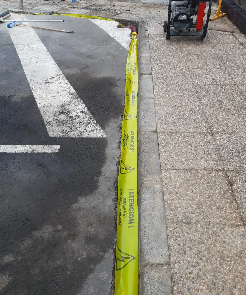 Canalización junto al bordillo de una acera con la cinta de señalización de cables eléctricos antes del cierre