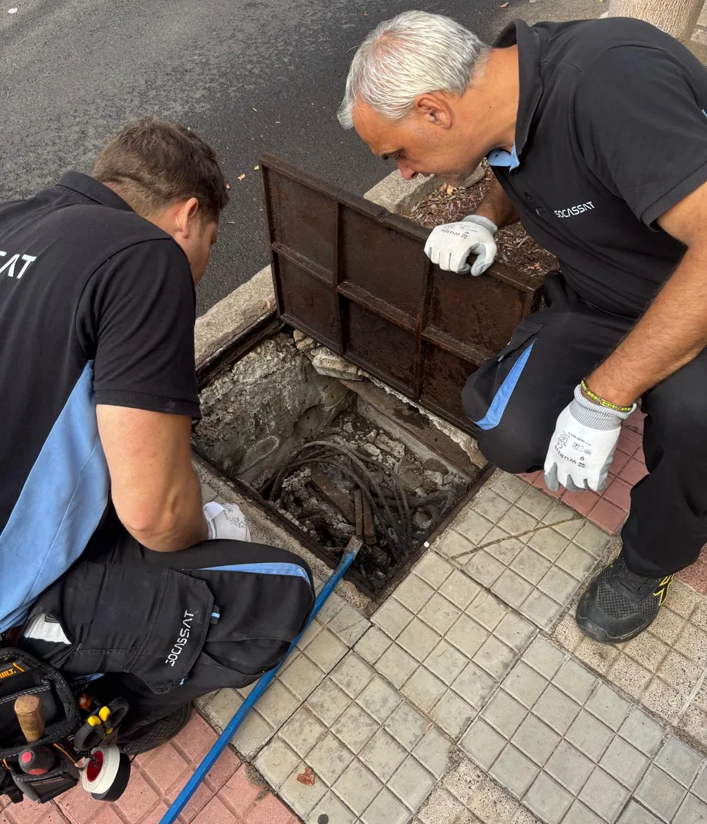 Dos técnicos de Socassat revisando el cableado de una arqueta en la acera