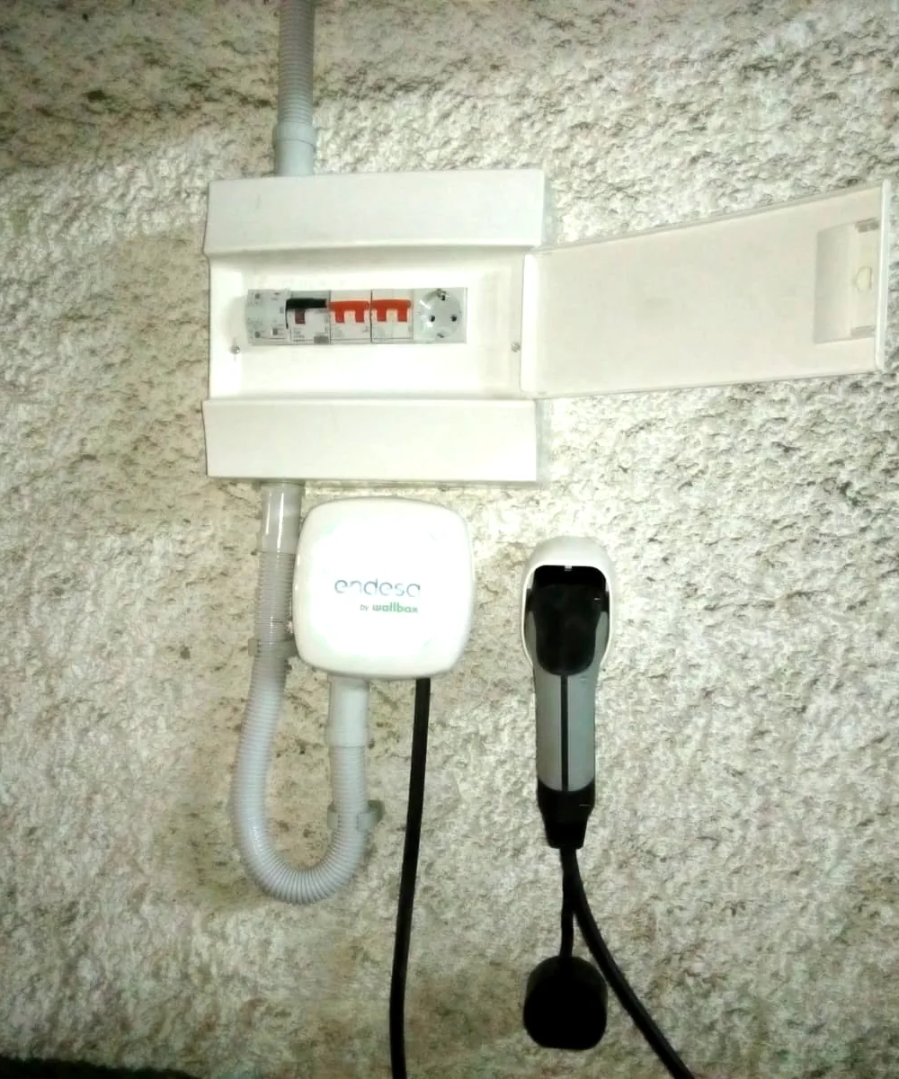 Cargador de coche eléctrico instalado en la pared exterior de una vivienda, junto a su cuadro de protecciones