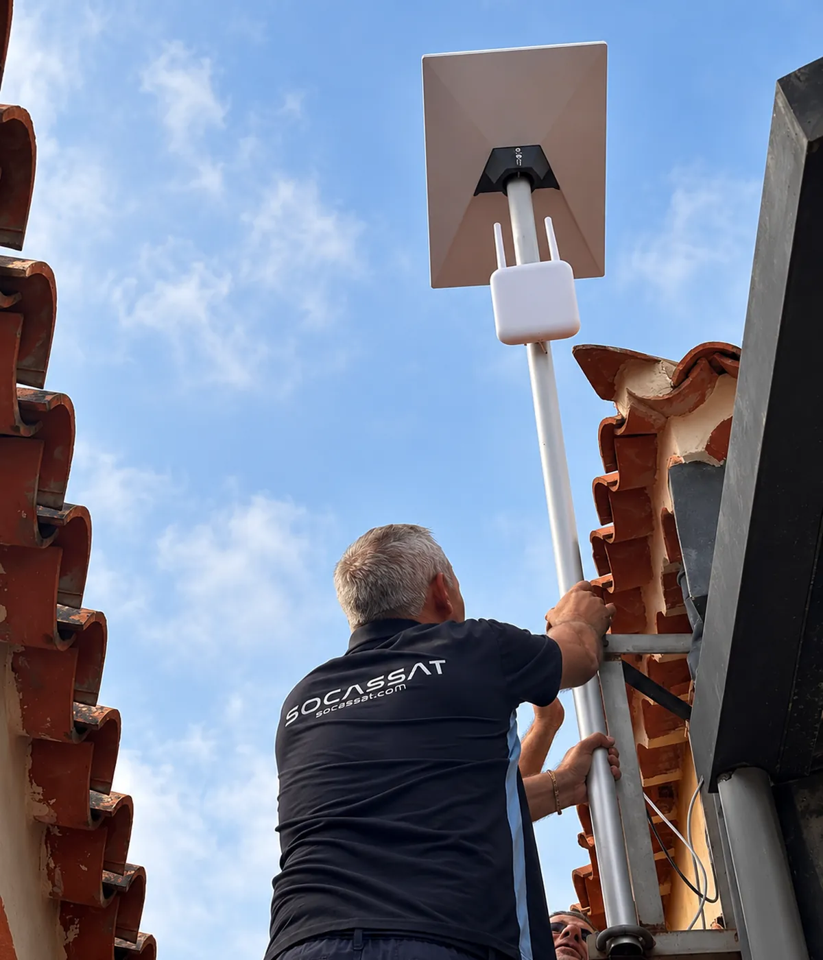 Técnico de Socassat fijando el mástil de una antena Starlink con un punto de acceso WiFi de exterior junto a un tejado de teja