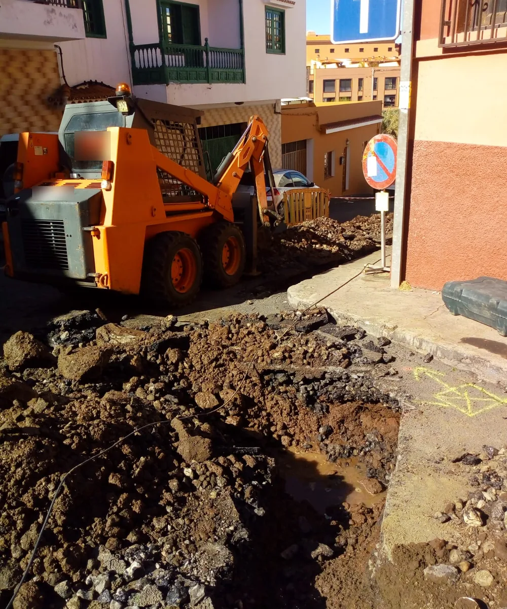 Apertura de una zanja en una calle de Tenerife con terreno volcánico, con la minicargadora y el vallado de la obra