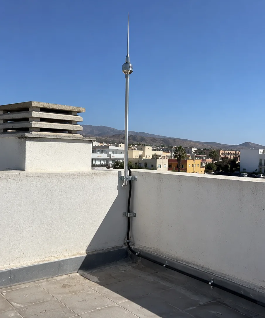 Pararrayos con dispositivo de cebado en la azotea de un edificio, con el bajante sujeto al peto