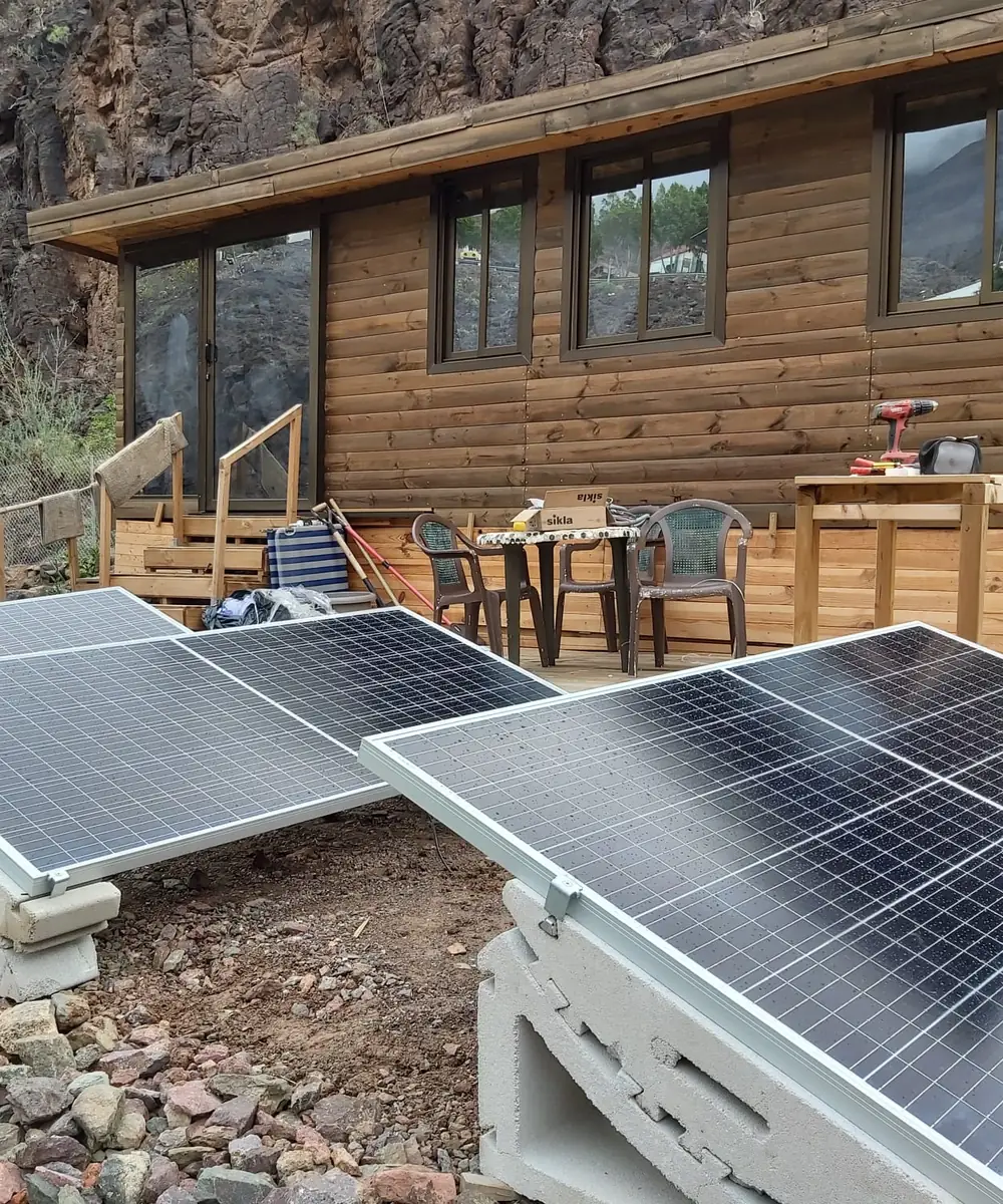 Placas solares sobre soportes de hormigón junto a una casa de madera en el campo