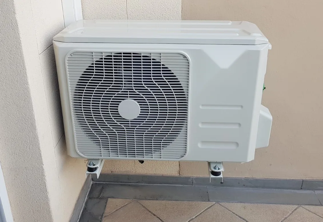 Unidad exterior de aire acondicionado instalada sobre soportes de pared con tacos antivibratorios en una terraza